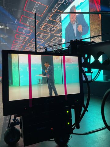 A monitor on a rolling stand in front of a red and blue stage set.