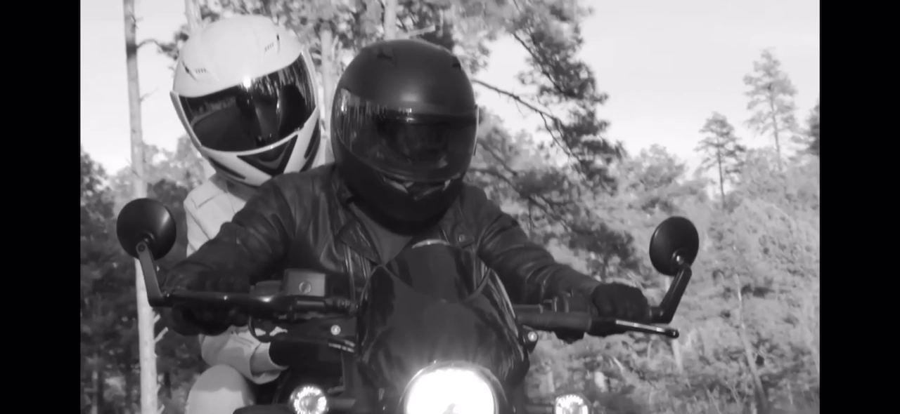 Brock Monroe, "Alien" — behind the scenes. A black-and-white frame: a rider in a black helmet and a passenger in a white helmet, riding between the trees.