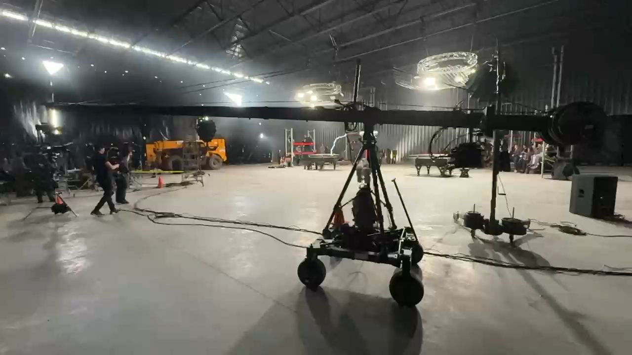 Behind the scenes, Tommee Profitt & William Joseph, "Thunderstruck" cover, music video (2024) — the Jib on its wheeled base in a dark soundstage, circular lights overhead and crew standing by before the take.